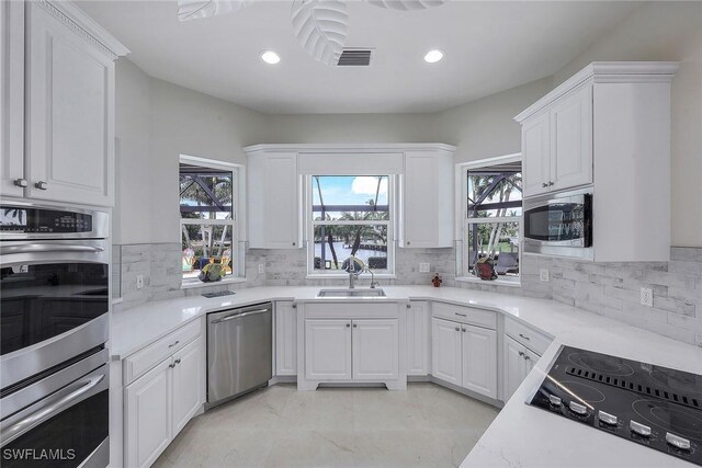 kitchen with light stone counters, white cabinets, sink, appliances with stainless steel finishes, and decorative backsplash