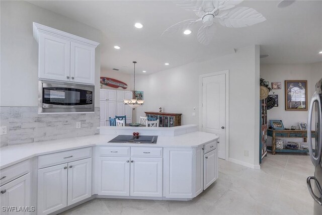 kitchen with white cabinetry, kitchen peninsula, stainless steel appliances, backsplash, and decorative light fixtures