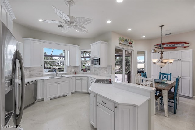 kitchen with white cabinets, ceiling fan with notable chandelier, kitchen peninsula, decorative light fixtures, and sink