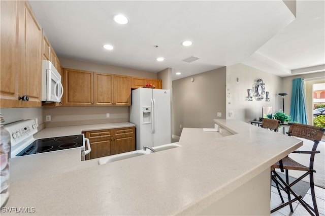 kitchen featuring a breakfast bar, white appliances, kitchen peninsula, light brown cabinetry, and sink