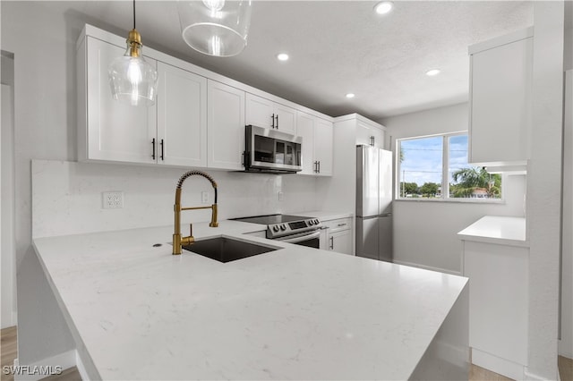 kitchen with pendant lighting, white cabinets, sink, kitchen peninsula, and appliances with stainless steel finishes