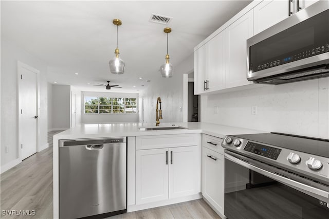 kitchen with appliances with stainless steel finishes, white cabinets, kitchen peninsula, ceiling fan, and sink