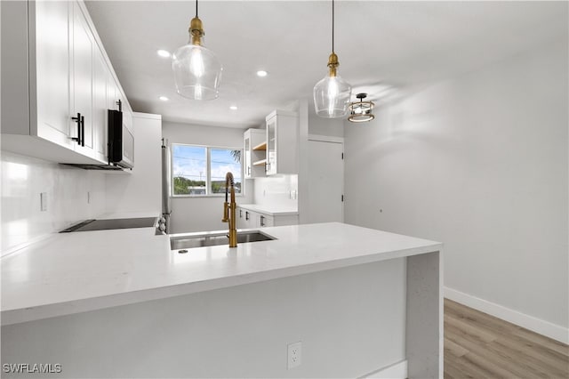 kitchen with white cabinets, hanging light fixtures, sink, kitchen peninsula, and light wood-type flooring