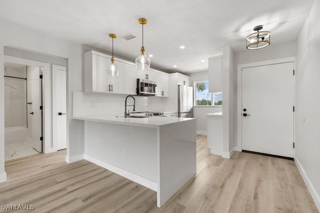 kitchen with white cabinets, kitchen peninsula, pendant lighting, stainless steel appliances, and light wood-type flooring