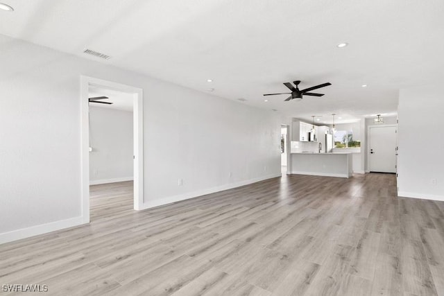 unfurnished living room with light wood-type flooring, sink, and ceiling fan