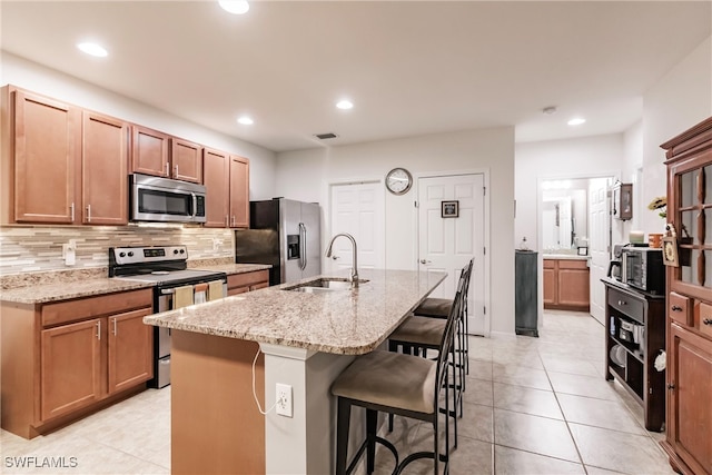 kitchen featuring a kitchen breakfast bar, an island with sink, light stone counters, stainless steel appliances, and sink