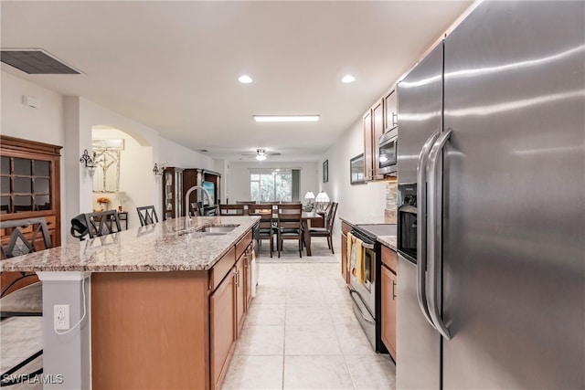 kitchen featuring appliances with stainless steel finishes, an island with sink, a kitchen bar, ceiling fan, and sink