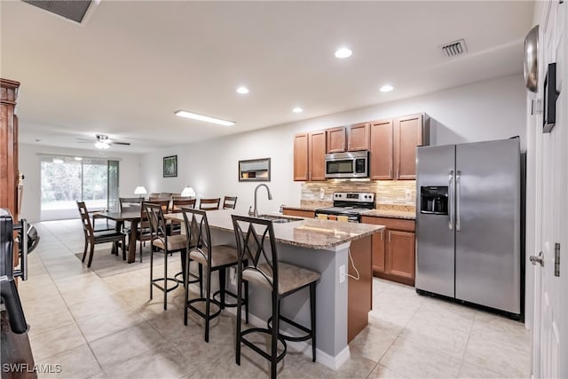 kitchen with appliances with stainless steel finishes, a breakfast bar area, ceiling fan, a kitchen island with sink, and sink