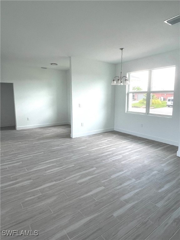 empty room with hardwood / wood-style floors and a notable chandelier