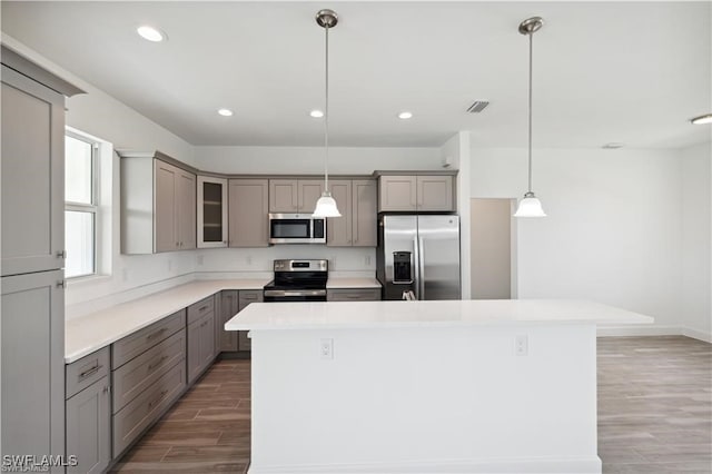 kitchen featuring appliances with stainless steel finishes, a kitchen island, hanging light fixtures, and dark hardwood / wood-style floors