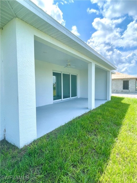 view of side of property featuring a lawn, ceiling fan, and a patio area