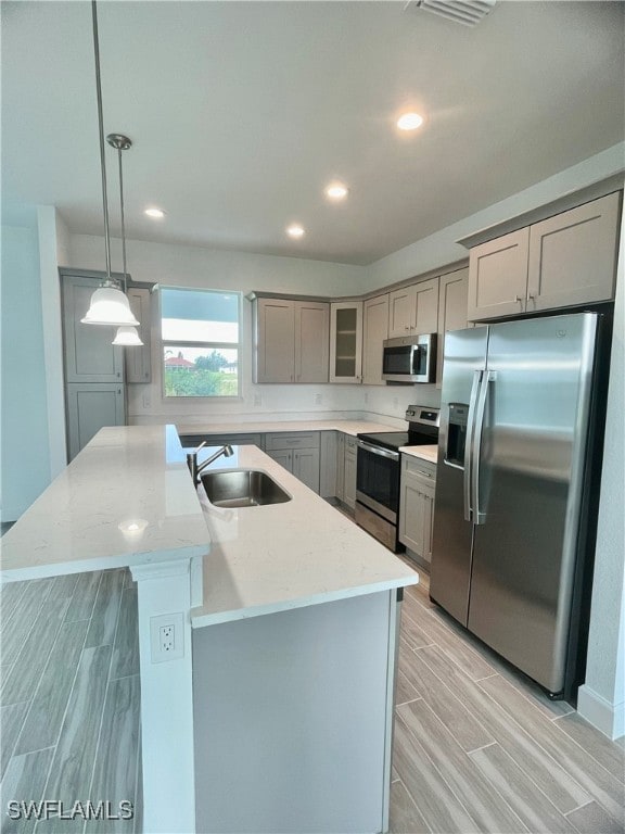 kitchen featuring hanging light fixtures, light hardwood / wood-style flooring, stainless steel appliances, sink, and a center island with sink