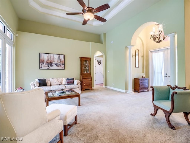 carpeted living room with a towering ceiling, a raised ceiling, ceiling fan, and ornate columns