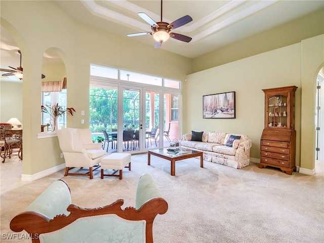 carpeted living room featuring a tray ceiling, ceiling fan, and a high ceiling