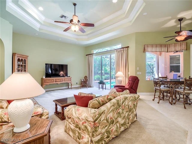 carpeted living room featuring ceiling fan, ornamental molding, a tray ceiling, and a wealth of natural light