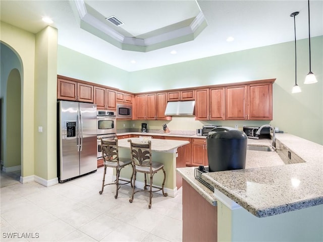 kitchen with light stone counters, decorative light fixtures, appliances with stainless steel finishes, a kitchen breakfast bar, and a high ceiling