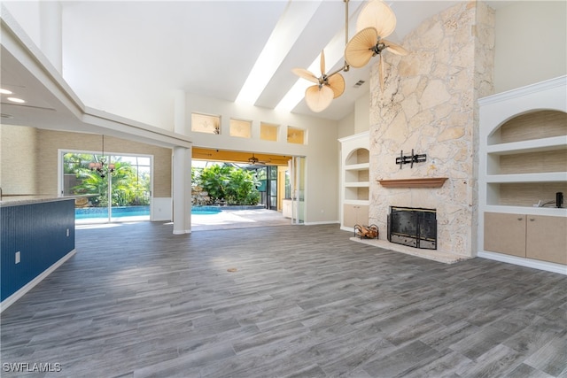 unfurnished living room featuring a stone fireplace, dark hardwood / wood-style floors, ceiling fan, and high vaulted ceiling