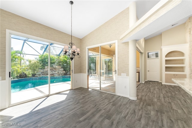 unfurnished dining area featuring built in shelves, an inviting chandelier, dark wood-type flooring, and high vaulted ceiling