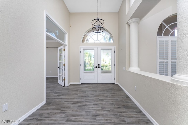 foyer entrance with a high ceiling, french doors, decorative columns, dark hardwood / wood-style floors, and a chandelier