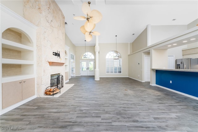 unfurnished living room featuring built in shelves, a stone fireplace, hardwood / wood-style flooring, and high vaulted ceiling