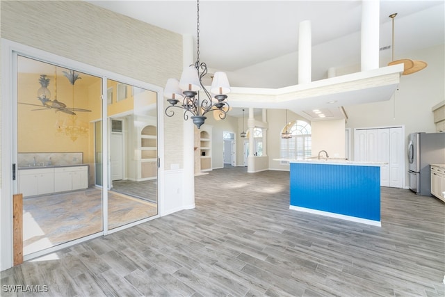 unfurnished dining area featuring wood-type flooring, an inviting chandelier, sink, and high vaulted ceiling