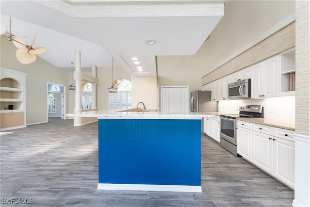 kitchen with white cabinets, decorative light fixtures, a kitchen island with sink, stainless steel appliances, and dark hardwood / wood-style floors