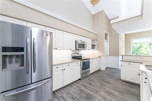 kitchen with light stone countertops, stainless steel appliances, white cabinetry, and light hardwood / wood-style floors