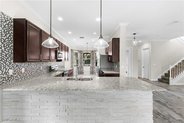 kitchen with light stone countertops, sink, kitchen peninsula, decorative light fixtures, and appliances with stainless steel finishes