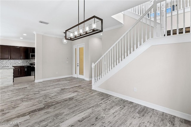 unfurnished living room featuring light wood-type flooring, crown molding, and a notable chandelier