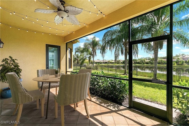 sunroom featuring ceiling fan and a water view