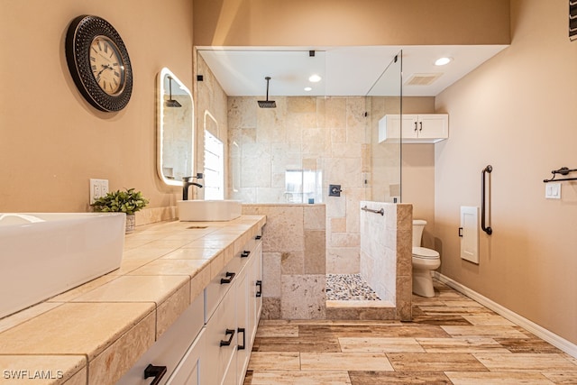 bathroom with a tile shower, vanity, toilet, and hardwood / wood-style flooring