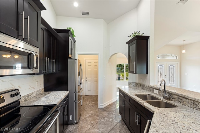 kitchen with sink, stainless steel appliances, light stone counters, backsplash, and pendant lighting