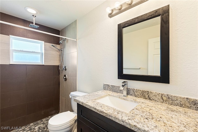 bathroom featuring a tile shower, vanity, and toilet