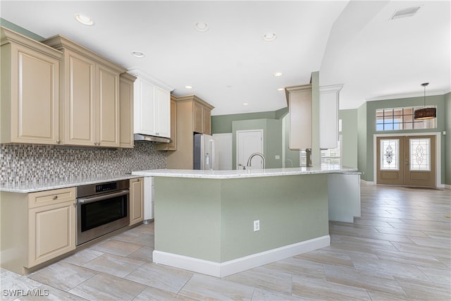 kitchen featuring decorative backsplash, white refrigerator with ice dispenser, light stone counters, stainless steel oven, and sink