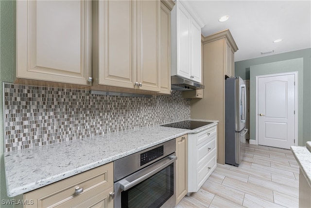 kitchen featuring light stone counters, cream cabinets, appliances with stainless steel finishes, and tasteful backsplash