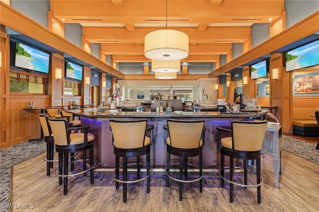 bar featuring a high ceiling, light hardwood / wood-style floors, wooden walls, and beam ceiling