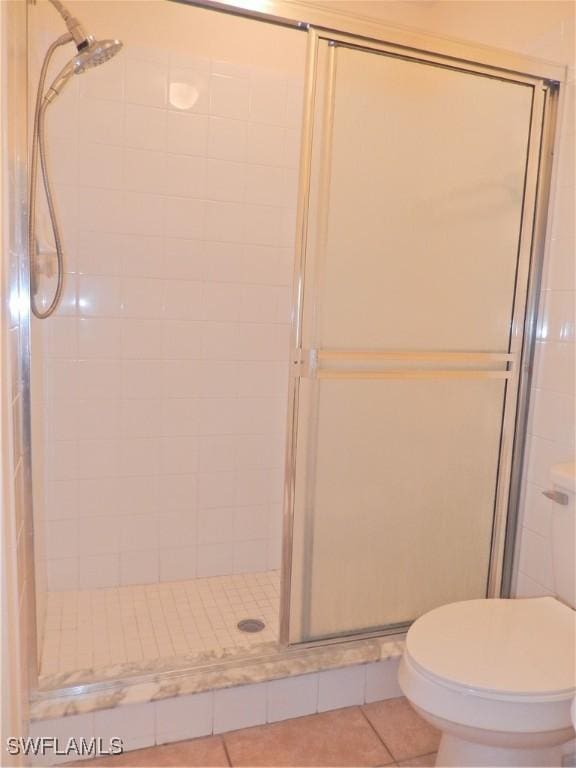 bathroom featuring toilet, tile patterned floors, and a shower with shower door