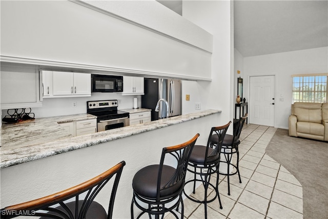 kitchen featuring light carpet, a kitchen breakfast bar, light stone counters, appliances with stainless steel finishes, and white cabinets