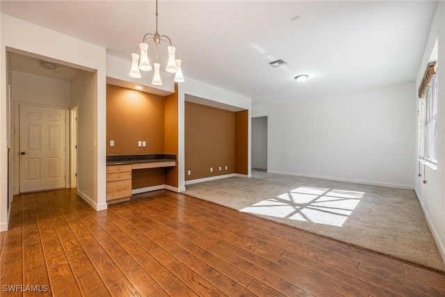 unfurnished room with a notable chandelier, wood-type flooring, and built in desk