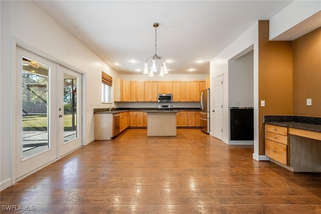 kitchen with appliances with stainless steel finishes, light wood-type flooring, a kitchen island, and hanging light fixtures