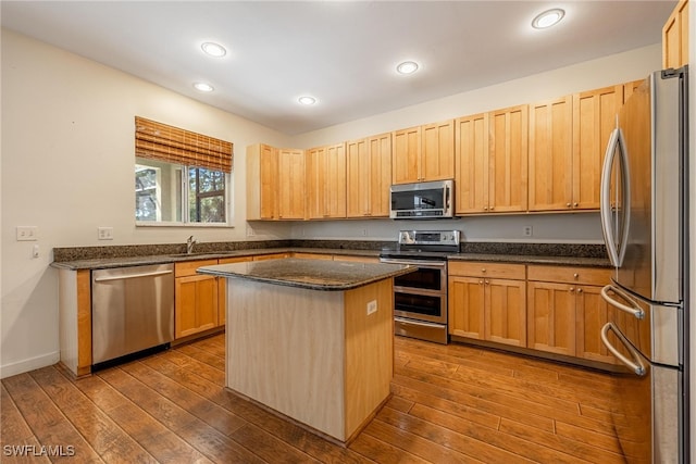 kitchen with stainless steel appliances, a kitchen island, hardwood / wood-style flooring, and dark stone countertops