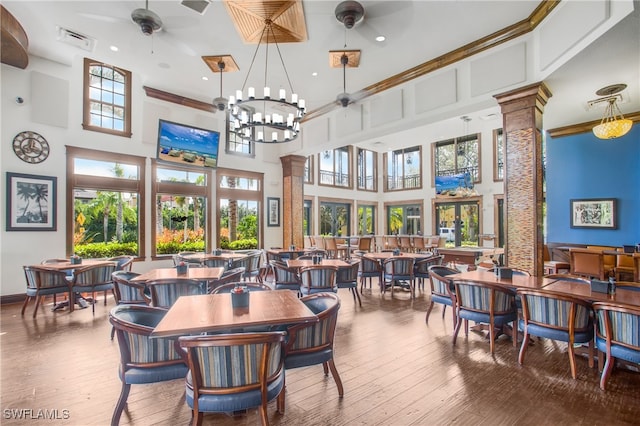 dining room featuring ceiling fan with notable chandelier, hardwood / wood-style floors, a towering ceiling, and ornate columns