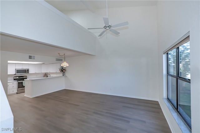 unfurnished living room featuring dark wood finished floors, visible vents, a towering ceiling, ceiling fan, and baseboards