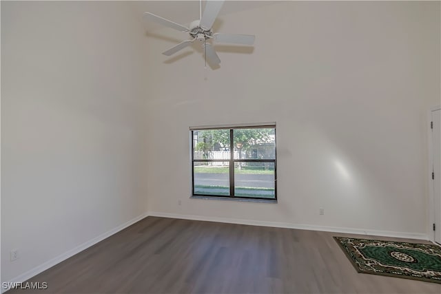 spare room with ceiling fan, dark wood-type flooring, a towering ceiling, and baseboards