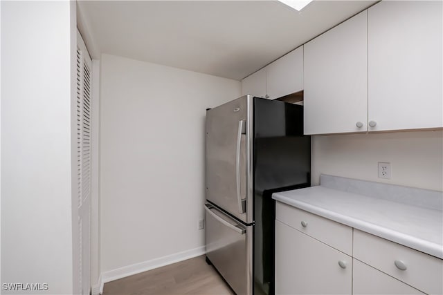 kitchen with white cabinetry, baseboards, light countertops, freestanding refrigerator, and light wood finished floors