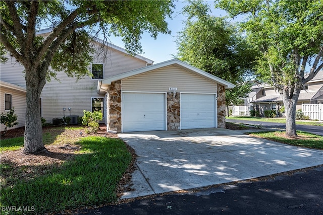 view of front of home with a garage, concrete driveway, stone siding, and central AC unit