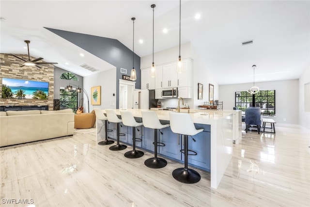 kitchen with ceiling fan, white cabinets, decorative light fixtures, a spacious island, and a kitchen bar