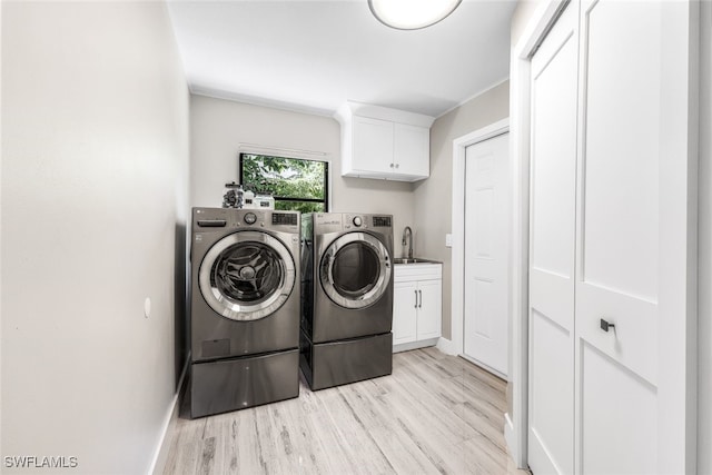 laundry room featuring washer and clothes dryer, cabinets, sink, and light hardwood / wood-style floors