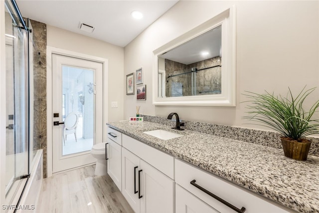 full bathroom with combined bath / shower with glass door, plenty of natural light, vanity, and toilet