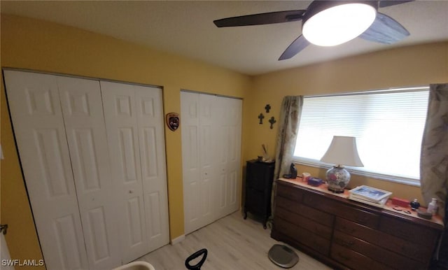 bedroom featuring ceiling fan, multiple closets, and light hardwood / wood-style flooring